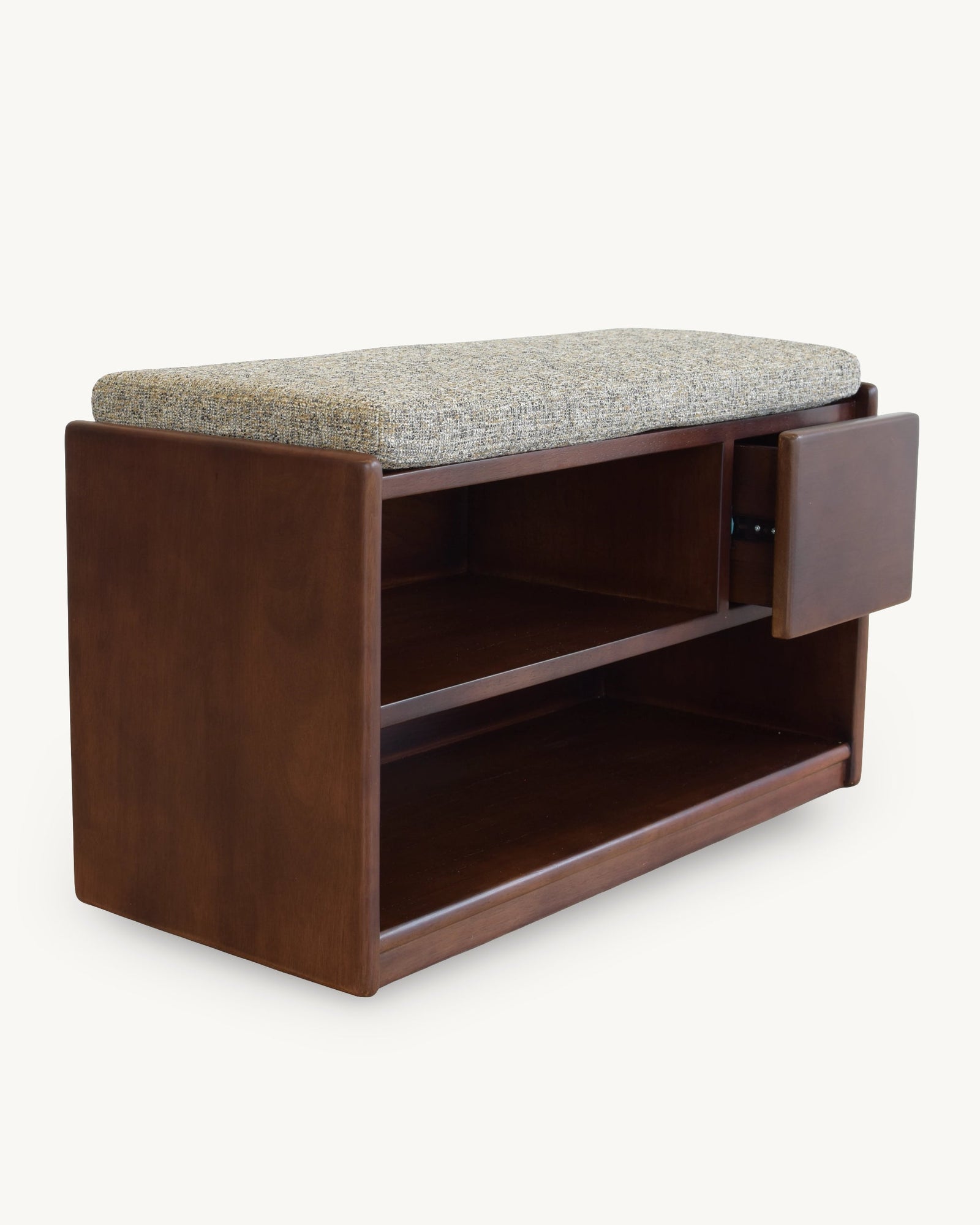 A mid-century modern wooden storage bench with a gray textured upholstered cushion on top, featuring a side-mounted cabinet door and open shelving, shown against a plain off-white background.
